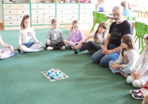 Dzieci siedzą na dywanie i słuchają o czym mówi nauczyciel