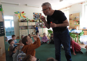 Nauczyciel puszcza bańki mydlane, dzieci próbują je złapać.