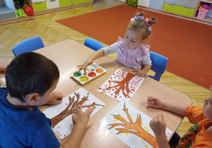 Dzieci malują farbami jesienne drzewa.