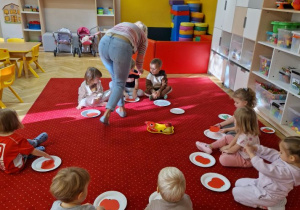 Dzieci siedzą na dywanie i układają papierowe jabłko złożone z dwóch części.