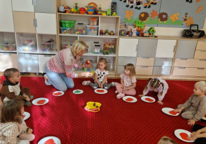 Dzieci siedzą na dywanie i układają papierowe jabłko złożone z dwóch części.