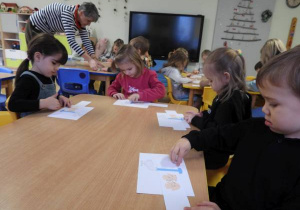 Dzieci wycinają nożyczkami przy stolikach.