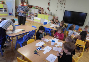 Dzieci wycinają nożyczkami przy stolikach.