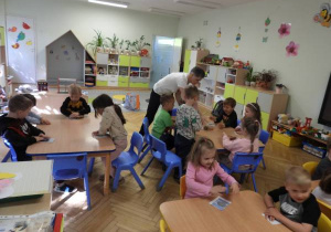 Dzieci siedzą na dywanie i uczestniczą w zajęciach Klubu Dociekliwego Przedszkolaka.
