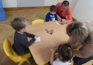 Dzieci siedzą na dywanie i uczestniczą w zajęciach Klubu Dociekliwego Przedszkolaka.