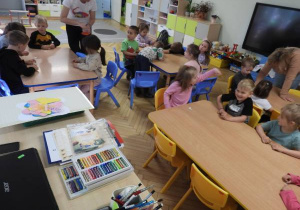 Dzieci siedzą na dywanie i uczestniczą w zajęciach Klubu Dociekliwego Przedszkolaka.