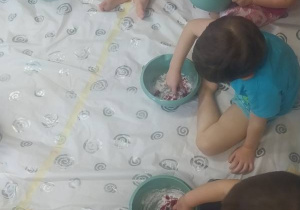 Dzieci siedzą na podłodze i lepią z masy plastycznej.