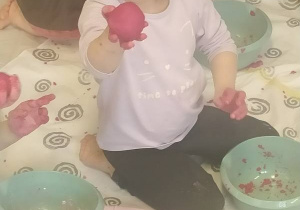 Dzieci siedzą na podłodze i lepią z masy plastycznej.