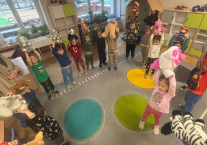 Dzieci siedzą na dywanie w kole. W rękach trzymają pluszowe maskotki.