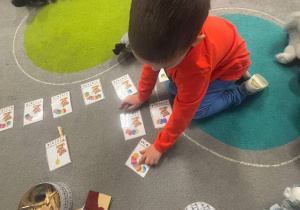 Chłopiec układa na dywanie kolorowe kartki.