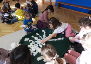 Dzieci siedzą na podłodze i zabarwiają watę na różne kolory.