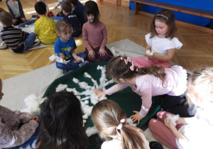 Dzieci siedzą na podłodze i zabarwiają watę na różne kolory.