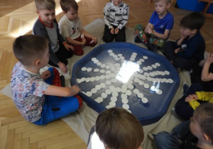 Dzieci siedzą na podłodze i zabarwiają watę na różne kolory.