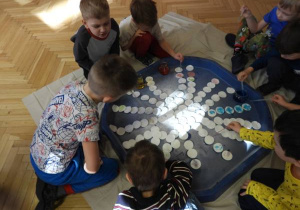 Dzieci siedzą na podłodze i zabarwiają watę na różne kolory.