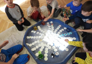 Dzieci siedzą na podłodze i zabarwiają watę na różne kolory.