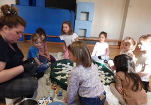 Dzieci siedzą na podłodze i zabarwiają watę na różne kolory.