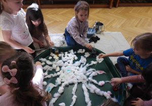 Dzieci siedzą na podłodze i zabarwiają watę na różne kolory.
