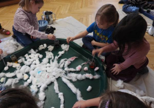 Dzieci siedzą na podłodze i zabarwiają watę na różne kolory.