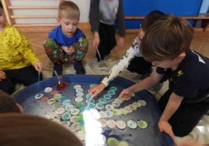 Dzieci siedzą na podłodze i zabarwiają watę na różne kolory.