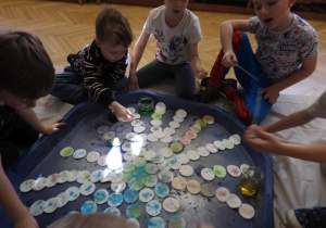 Dzieci siedzą na podłodze i zabarwiają watę na różne kolory.