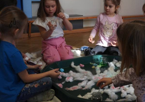 Dzieci siedzą na podłodze i zabarwiają watę na różne kolory.