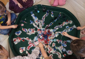 Dzieci siedzą na podłodze i zabarwiają watę na różne kolory.