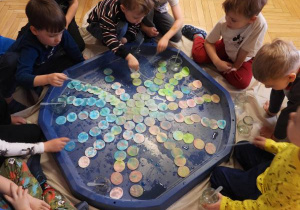 Dzieci siedzą na podłodze i zabarwiają watę na różne kolory.